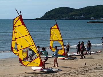 浜辺でウィンドサーフィンをしようと女性がボードの上に乗っている写真