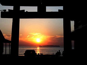 手前に鳥居があり奥には海に沈む夕日が写っている写真