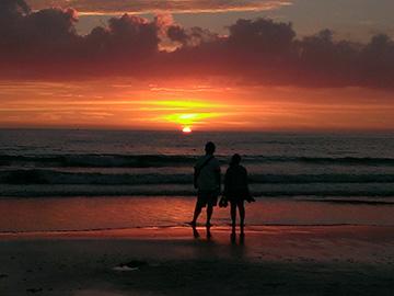 海に沈んでいく夕日を男性と女性が並んで眺めている写真