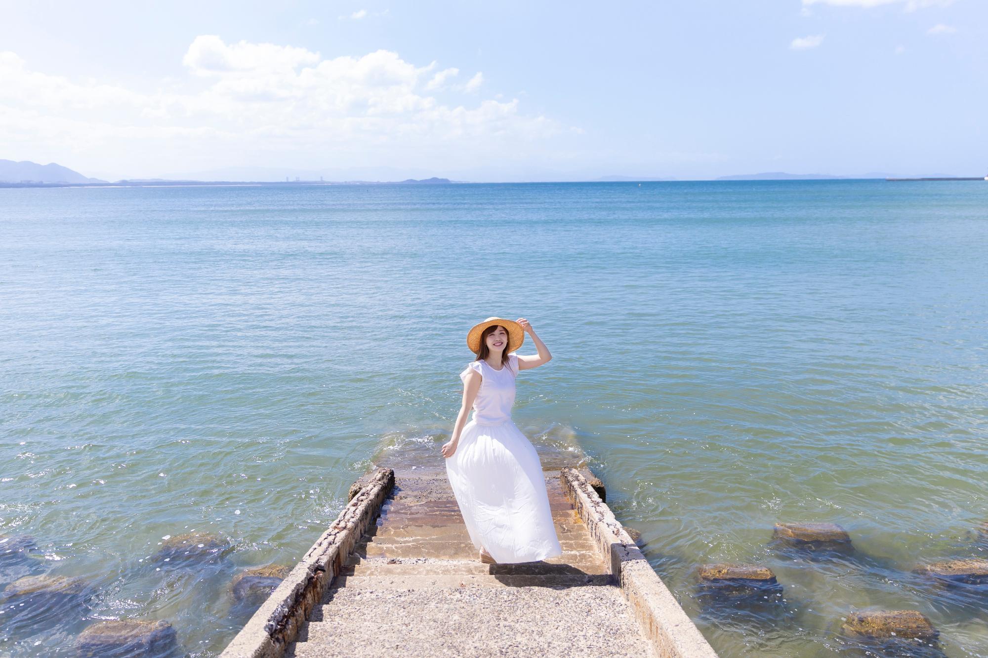 津屋崎海岸を背景に白い服を着てこっちを向く新木さくらさん