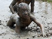 泥の中で全身泥まみれの子どもが四つん這いになっている写真