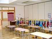 机が6台ほど置いてあり、後ろには子供たちの荷物が置いてある教室の写真