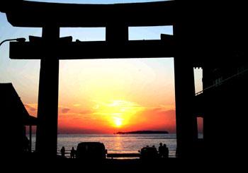 鳥居の間から夕日が赤々と宮地浜を照らしている写真