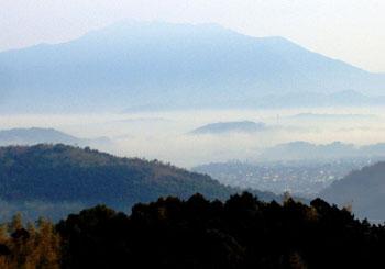 山々に雲がかかり中央に住宅地がある冠山の山頂から見渡す風景写真