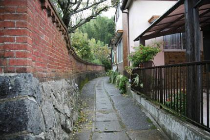 左側に赤いレンガ造りの塀が細い歩道に沿って奥へと続いている写真