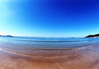 真っ青な海で静かなさざ波が立っている津屋崎海岸の写真