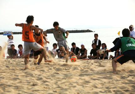 男性たちによるビーチサッカーで3名の選手がボールを取ろうと競っている写真
