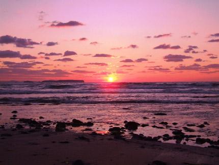 地平線に夕日が沈もうとしている赤色に染まった空と海の写真
