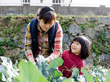女の子とお母さんが畑の野菜を手入れしている写真