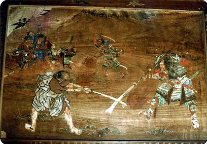 木の板に刀を持った武士2人が戦っている姿が描かれている曽我兄弟図の写真