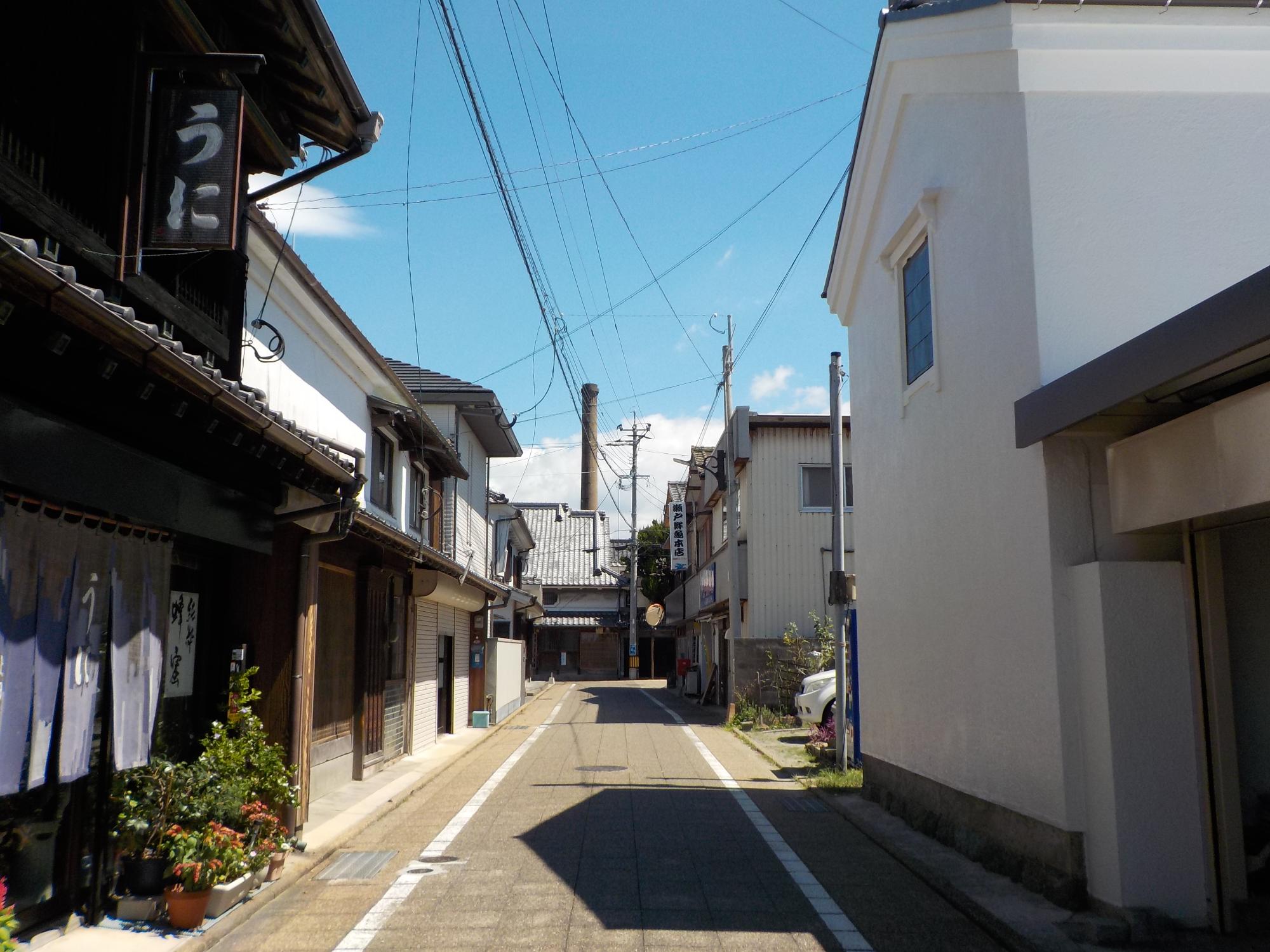 昔ながらの古い建物が連なる道の最奥に煙突が建っている写真