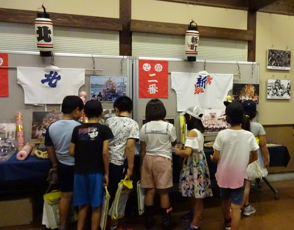 展示コーナーに飾られた津屋崎祇園山笠の写真や法被などを熱心に見つめる小学生たち