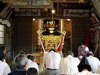 神社の中ではお神輿が前に置かれ、その後ろに人が正座して頭を下げている写真