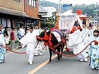 黒い被り物をし、白い衣装を着た男性が馬を引き連れており、両隣には十二単姿の女性が馬の鼻についている赤い紐を持ちながら歩いている写真