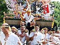白い着物を着た男性方が人形が飾られている神輿を担いでいる写真