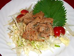 白いお皿にキャベツなどがのせられその上に豚肉のスタミナソースかけ,飾りにシソの葉ミニトマトがのった料理の写真