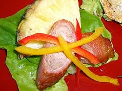 サラダ菜の敷かれた器に豚もも薄切り肉の肉巻きとパイナップルとピーマン(赤・黄)が盛り付けられている写真
