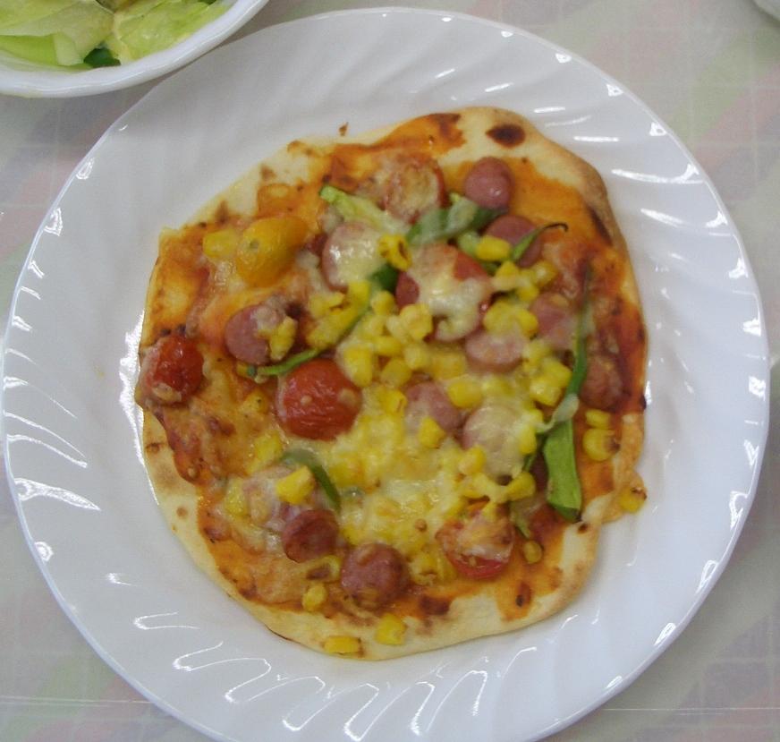 白いお皿に盛られたピーマンやコーン、ミニトマト、ベーコンでつくった丸いピザの写真