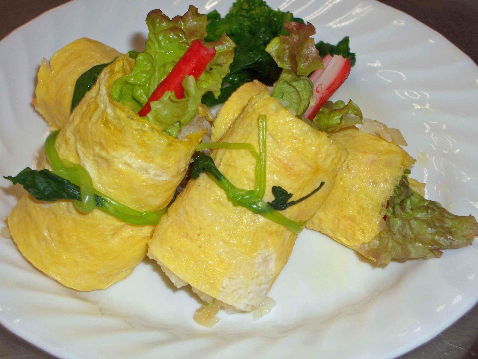 寿司飯、かにかま、サニーレタスを薄焼き卵で巻き、三つ葉で結んだお寿司がお皿に盛られている写真